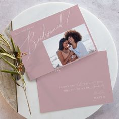 two pink wedding thank cards on top of a white plate with flowers and greenery