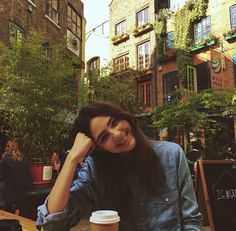 a woman sitting at a table with a cup of coffee in front of her smiling