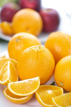 several oranges on a plate with apples in the background