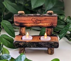 two candles are sitting on a wooden bench next to some plants and greenery with hearts drawn on it