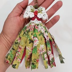 a hand holding a small doll with flowers on it's dress and red shoes