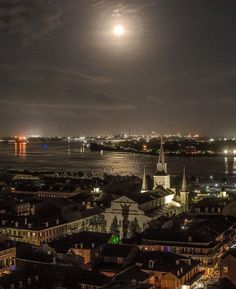 the full moon shines brightly in the night sky over an urban area with water and buildings