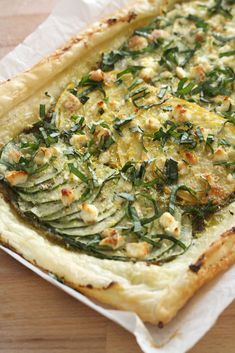 a vegetable quiche with cheese and spinach is on a white paper wrapper