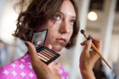 a woman holding a brush and eyeshade in front of her face