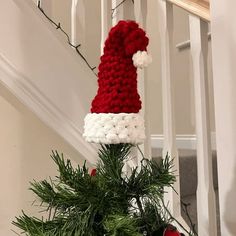 a knitted santa hat sitting on top of a christmas tree next to a banister