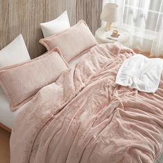 a bed with pink comforter and pillows on top of it next to a window