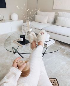 a person in white sweater and slippers sitting at a glass table with coffee cup