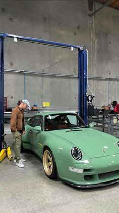 a man standing next to a green sports car in a garage with other people working on it