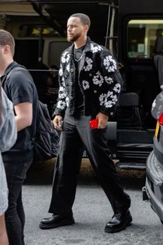 a man in black and white jacket walking next to a car with people standing around