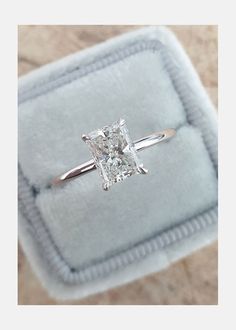 an engagement ring with a princess cut diamond set in 18k white gold on a velvet box