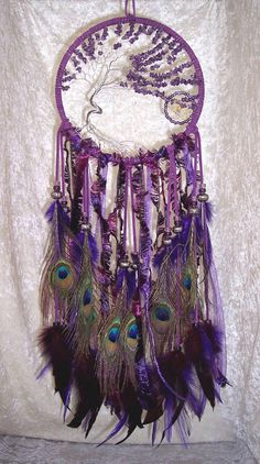 a purple dream catcher with feathers hanging from it's side on a white wall