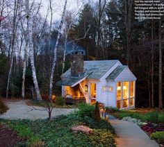 a small white house surrounded by trees and bushes at night with lights on the windows