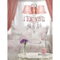 a pink chandelier hanging from the ceiling in a room with white furniture and curtains