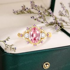 a pink tourmaline ring sitting on top of a green box next to flowers