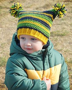 a young boy wearing a green and yellow hat with pom poms on it