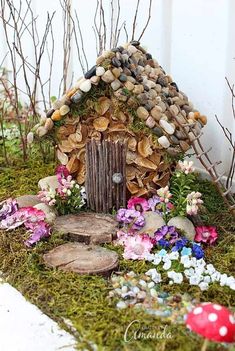 a fairy house made out of wood and rocks with flowers around the front door area