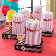 popcorn bags and cups on a table with balloons in the background