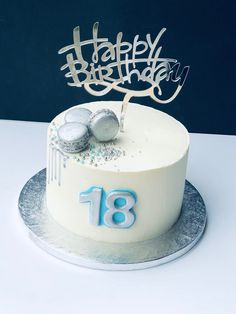 a white frosted birthday cake with blue icing and two silver balls on top