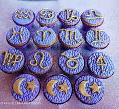 purple cupcakes with gold icing decorated with zodiac signs and stars on them