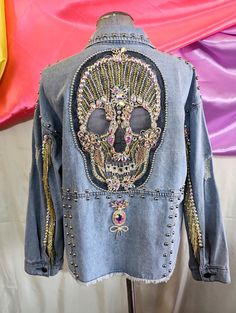 a denim jacket with beaded and sequins on the back is displayed in front of a colorful backdrop