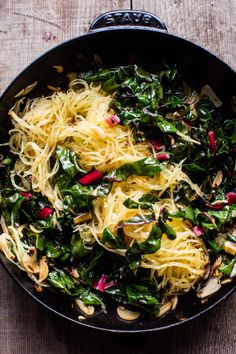 a pan filled with pasta and greens on top of a wooden table