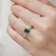 a woman's hand wearing a ring with an emerald and diamonds