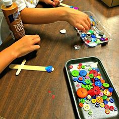 two children sitting at a table with buttons and glue on the table next to them