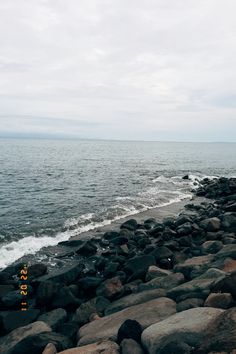 a rocky beach next to the ocean under a cloudy sky