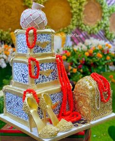 an elaborately decorated wedding cake with red and gold decorations on display in a garden