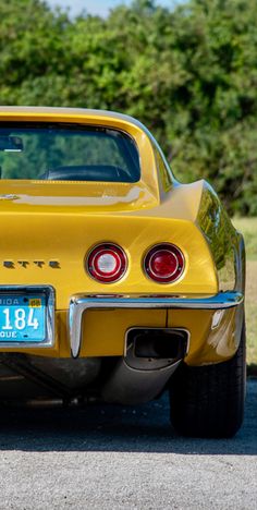 an old yellow car is parked on the side of the road with trees in the background