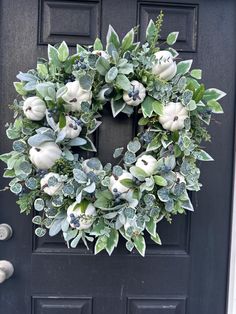 a wreath with white flowers and green leaves is hanging on the front door's black door