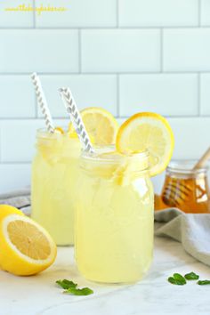 two mason jars filled with lemonade sitting on top of a counter next to sliced lemons