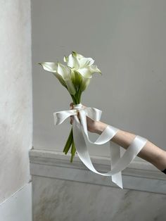 a person holding a bouquet of flowers with white ribbons tied around the stems in front of them