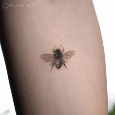 a small bee tattoo on the back of a woman's thigh, it is black and grey