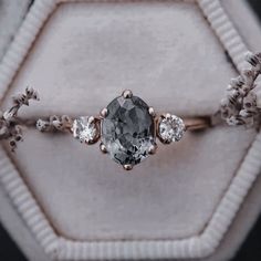 an engagement ring with a large gray diamond surrounded by smaller white diamonds in a hexagonal box