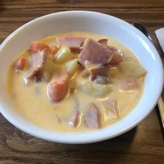 a white bowl filled with soup on top of a wooden table next to a fork