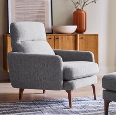 a chair and ottoman in a living room with a vase on the wall behind it