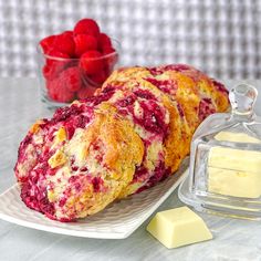 raspberry scones on a plate next to butter and some strawberries in a glass container