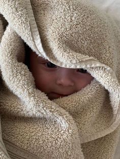 a young child wrapped in a blanket and looking at the camera with one eye open