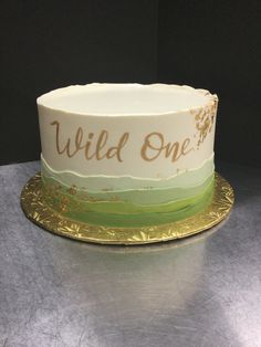 a white and green cake with the words wild one on it sitting on a gold plate