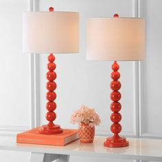 two red lamps sitting on top of a white table next to a vase with flowers