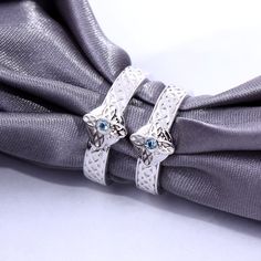 two silver rings sitting on top of a gray tie with blue stones in the middle