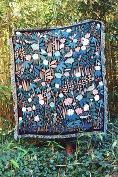 an old quilt is hanging on a tree stump in the woods, with flowers and leaves all over it