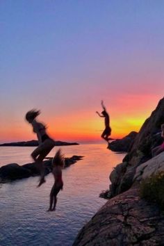 people jumping off rocks into the water at sunset