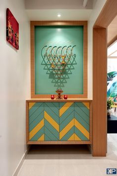 a green cabinet with yellow and blue chevrons in front of a painting on the wall