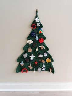 a crocheted christmas tree hanging on the wall in front of a white wall