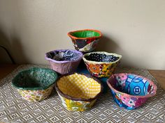 several different colored bowls sitting on top of a woven table cloth covered table with white wall in the background