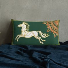 a green and gold pillow with a white horse on the front sitting on a bed