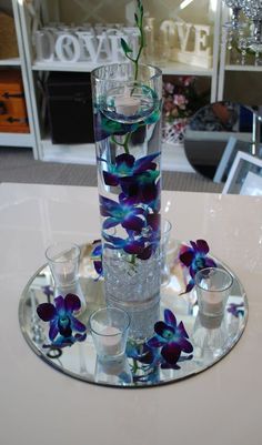 a glass vase filled with purple flowers on top of a white table next to glasses