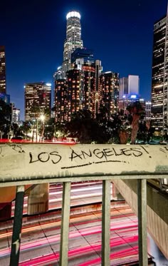 the city skyline is lit up at night, with graffiti on the fence and buildings in the background